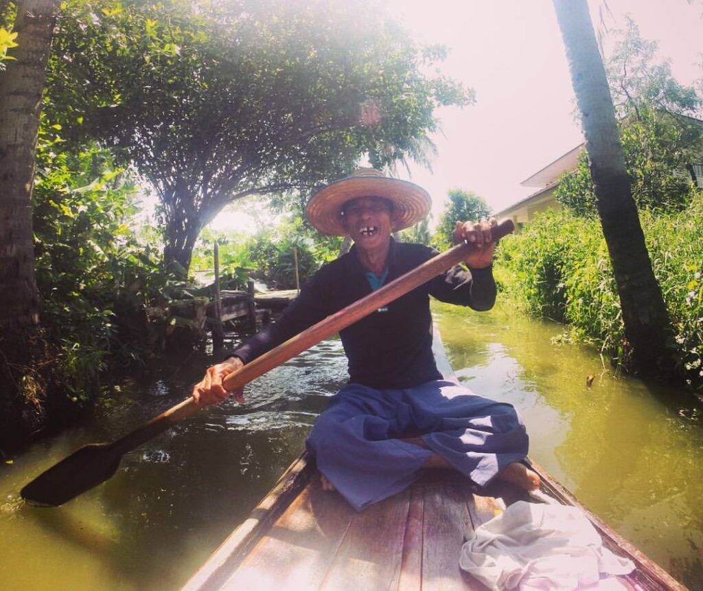 Senhor que rema e direciona o barco entre os canais do Khlong Lat Mayom, mercado flutuante em Bangkok